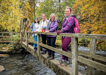 A group of Contours staff, bundled up in our late autumn outdoor kit, stand on a bridge over a river in the Peak District.