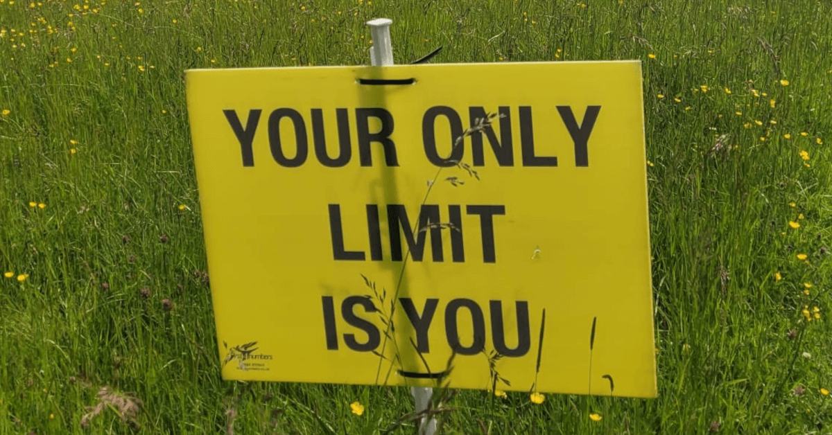A yellow sign in the grassy verge of a running trail reads YOUR ONLY LIMIT IS YOU.