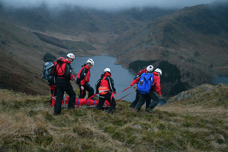 Mountain Rescue carry a stretcher over hilly land.