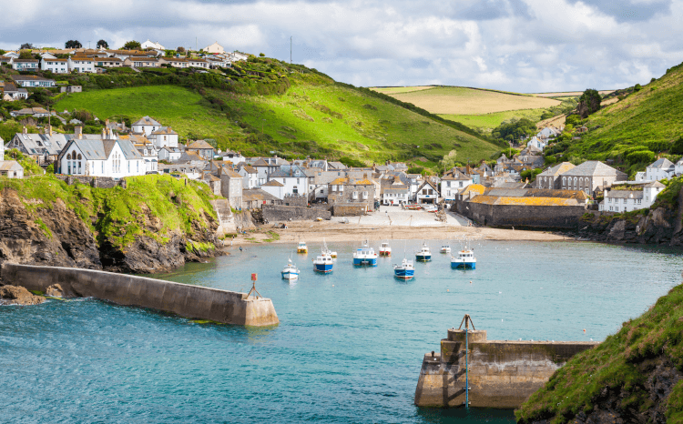 A view from a boat across the harbour to the white buildings clustered along the shoreline of Port Isaac.